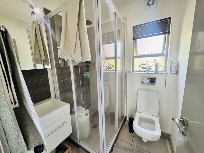 A compact, modern bathroom featuring a glass-enclosed shower, wall-mounted toilet, and a sleek vanity basin with tiled finishes.