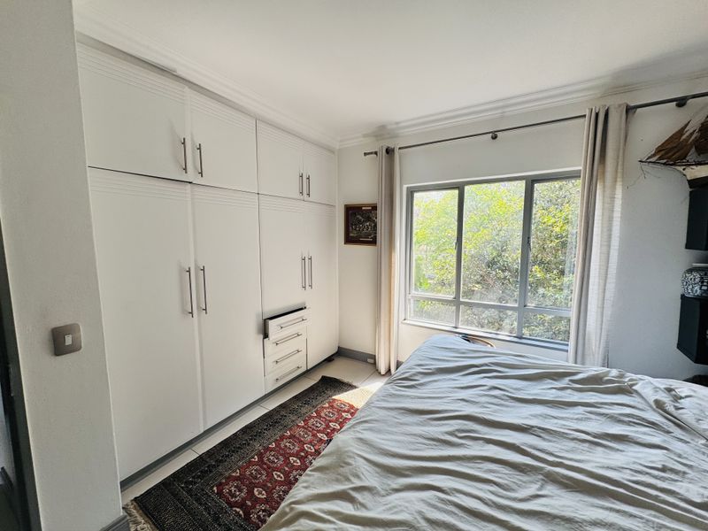 A well-lit bedroom featuring extensive floor-to-ceiling built-in cupboards and a large window overlooking greenery.
