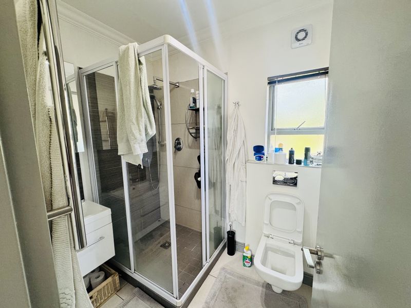 A compact, modern bathroom featuring a glass-enclosed shower, wall-mounted toilet, and a sleek vanity unit with neutral tiling.