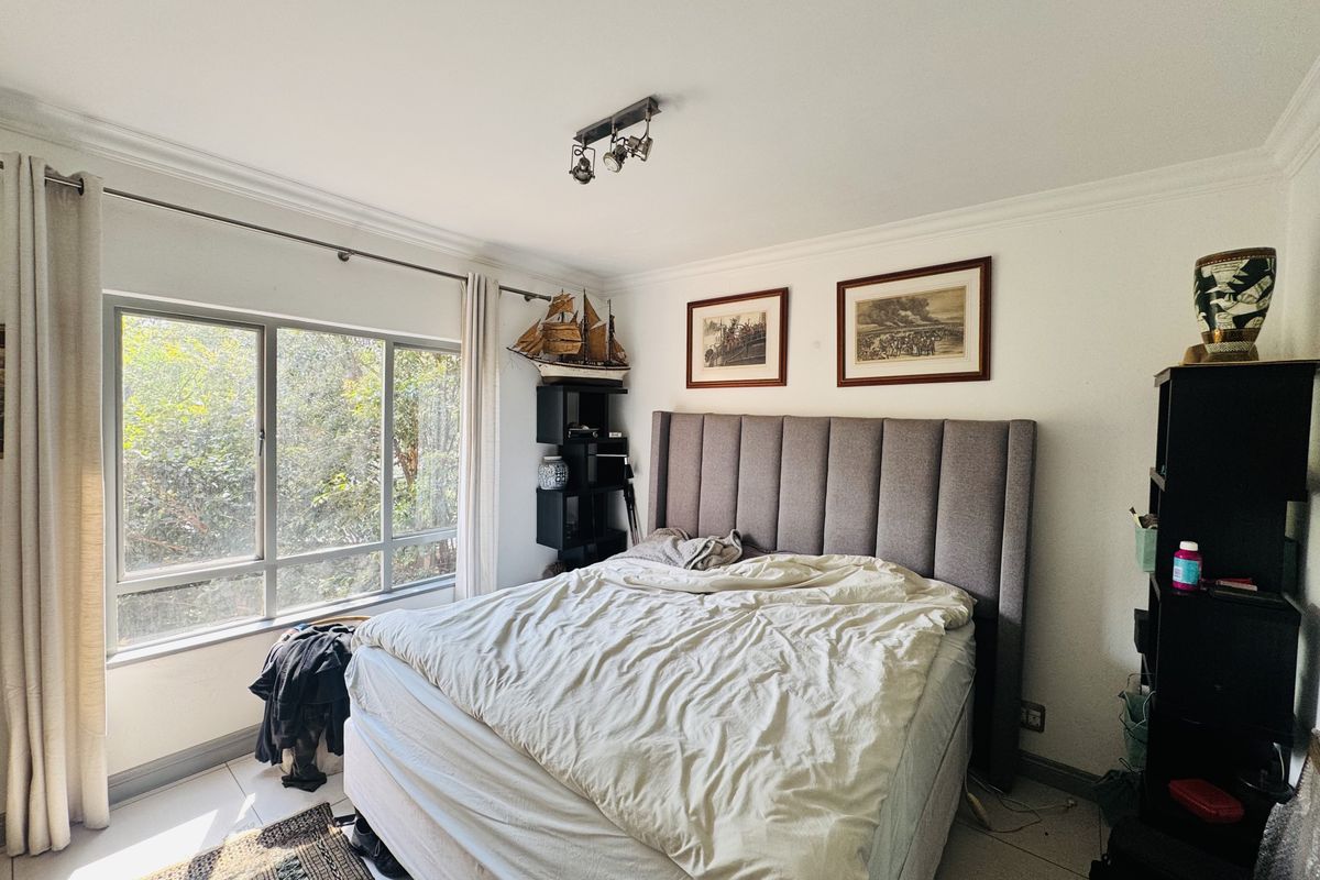 A well-lit bedroom featuring tiled flooring, a large window with natural light, and neutral wall finishes.