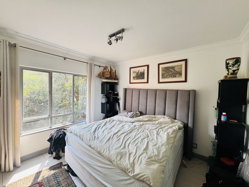 A well-lit bedroom featuring tiled flooring, a large window with natural light, and neutral wall finishes.
