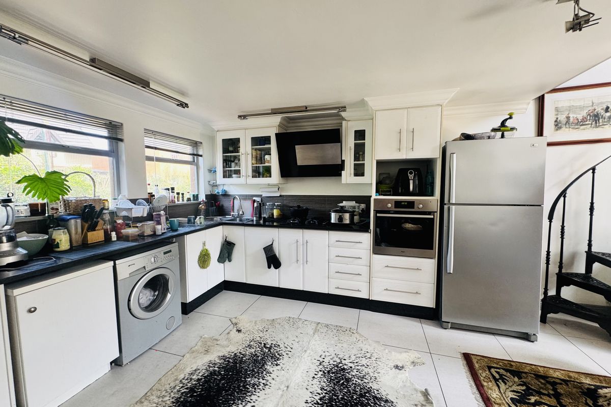 A functional kitchen featuring white cabinetry, dark countertops, integrated oven, extractor fan, and tiled flooring with space for laundry appliances.