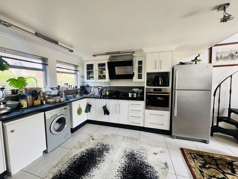 A functional kitchen featuring white cabinetry, dark countertops, integrated oven, extractor fan, and tiled flooring with space for laundry appliances.