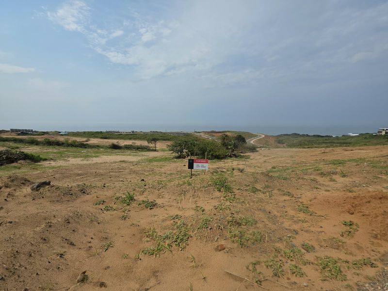 A vacant residential plot of land featuring natural coastal terrain and distant ocean views, ideal for custom home development.