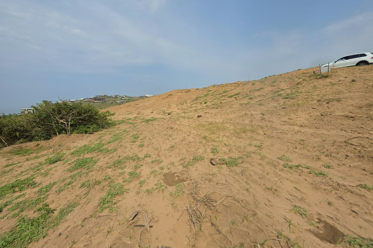 A view of a sloped, undeveloped residential plot featuring sandy terrain and natural vegetation, offering potential for future construction.