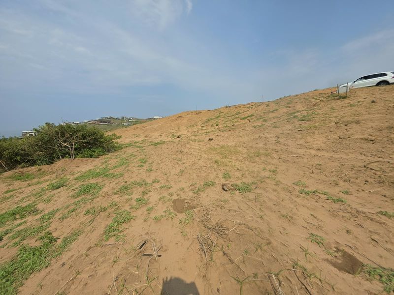A view of a sloped, undeveloped residential plot featuring sandy terrain and natural vegetation, offering potential for future construction.