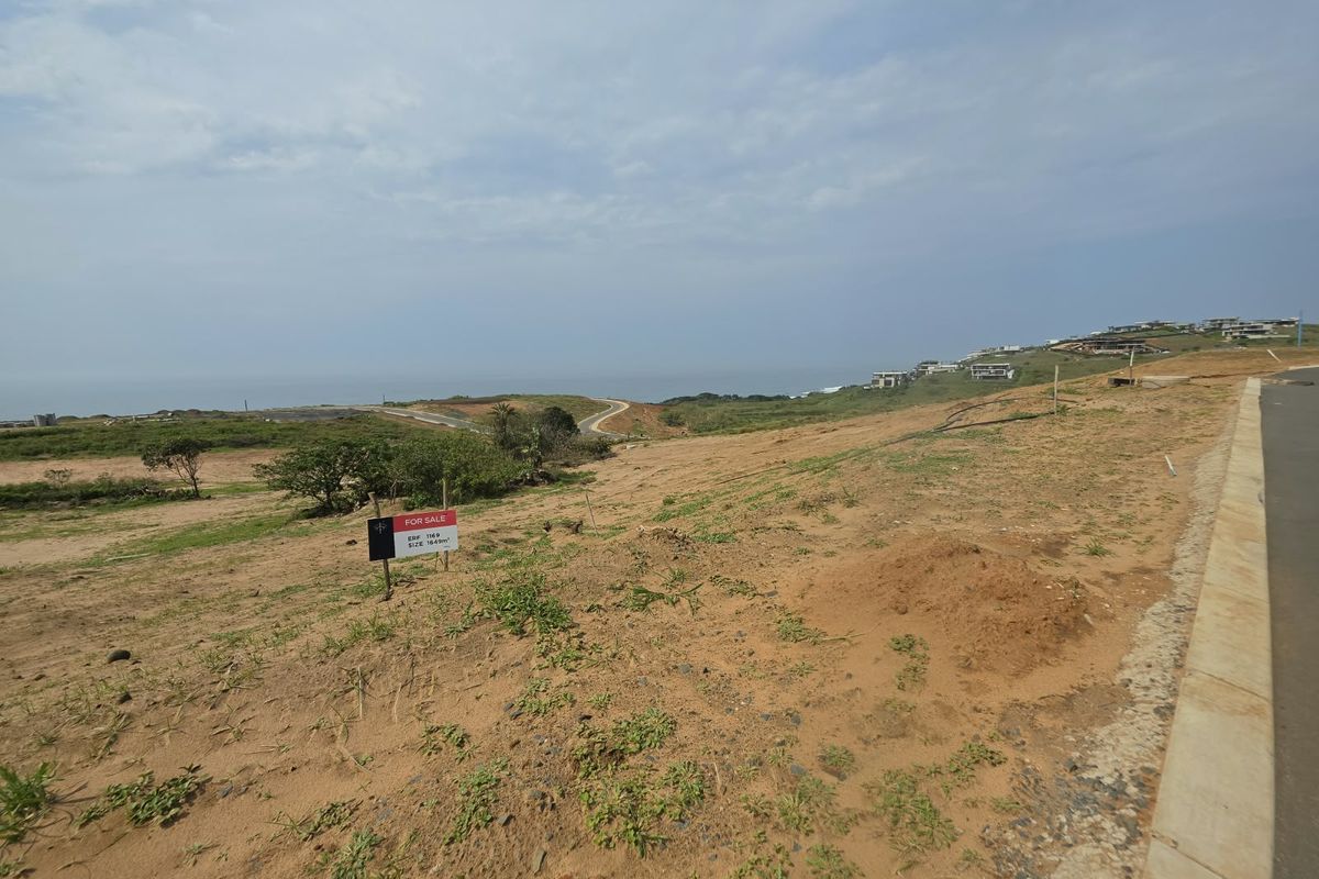 A vacant residential plot featuring a gentle slope, paved road access, and expansive coastal views in a developing estate.