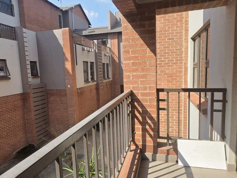 A private balcony featuring tiled flooring, a metal balustrade, and exposed brick walls, overlooking the complex courtyard area.