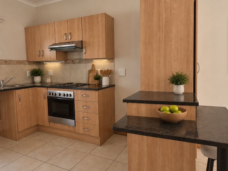 A functional kitchen featuring light wood-finish cabinetry, dark laminate countertops, a built-in oven with gas hob, and tiled flooring.