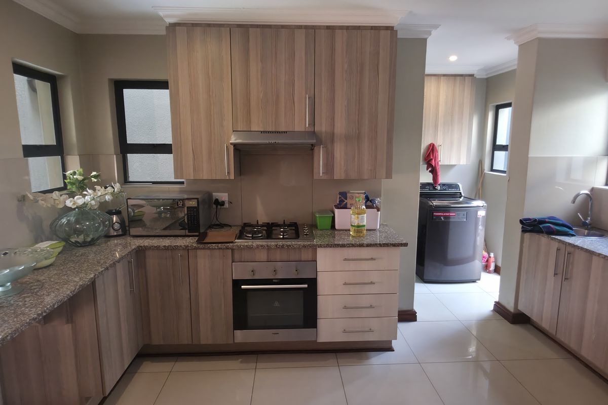 Modern kitchen featuring wood-finish cabinetry, granite countertops, built-in gas hob, oven, extractor fan, and tiled flooring, with an adjacent laundry area.