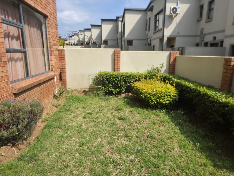 A private rear garden area featuring a small lawn, established hedging, and brick boundary walls, adjacent to the townhouse exterior.