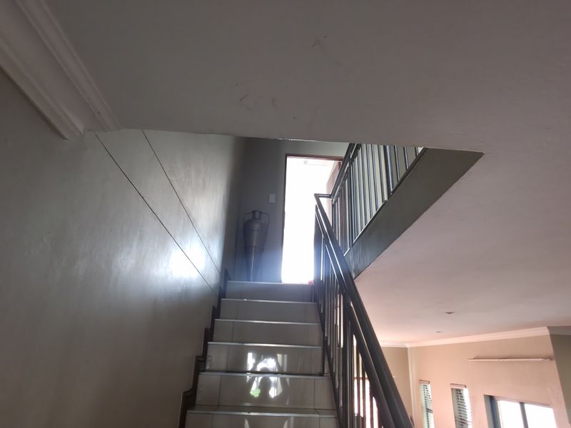 A staircase with tiled steps and a metal balustrade leading to an upper level, featuring recessed lighting and neutral wall finishes.
