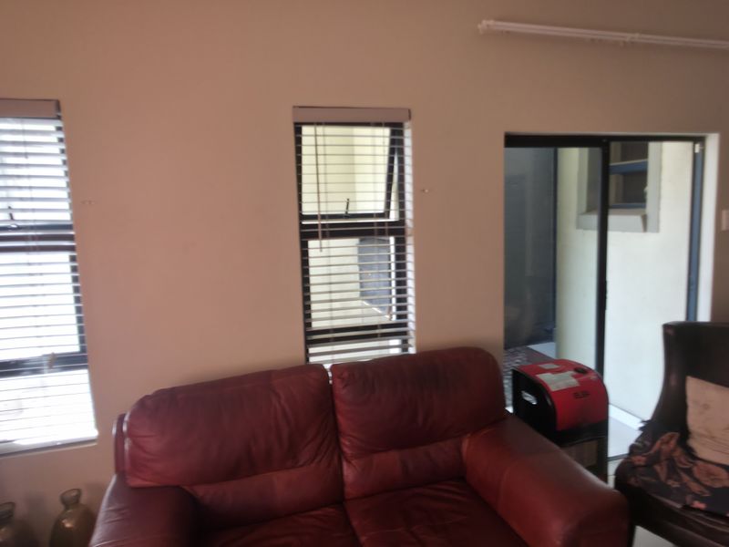 Open plan living area featuring aluminium windows with venetian blinds, a sliding door to the exterior, and a view into the adjacent kitchen.
