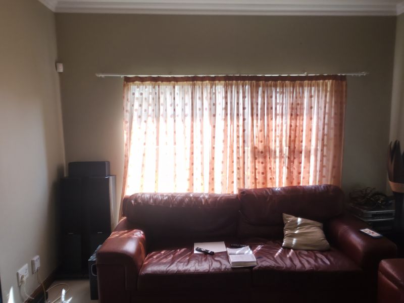 A living room featuring neutral wall tones, crown molding, and window treatments including venetian blinds and curtains.