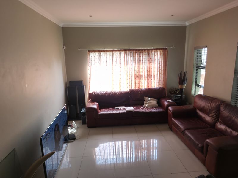 A spacious living room featuring neutral wall tones, polished tiled flooring, and large windows with venetian blinds, providing a bright and functional living space.