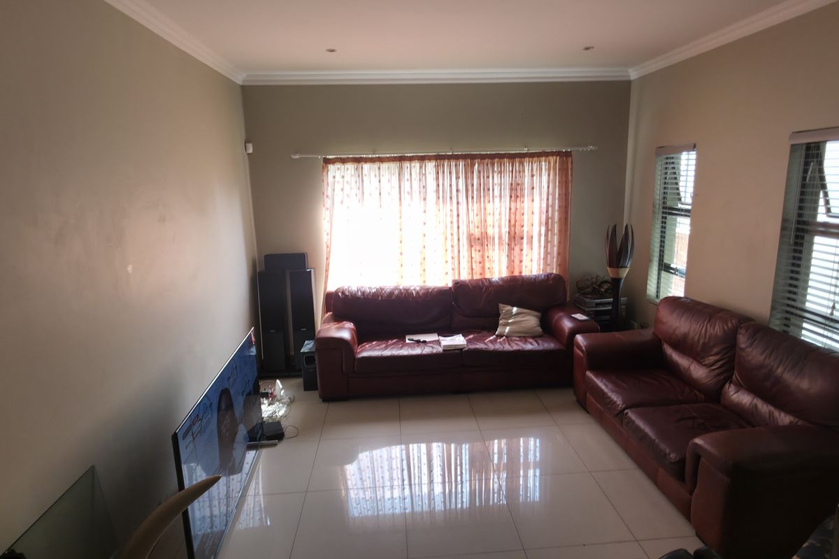 A spacious living room featuring neutral wall tones, polished tiled flooring, and large windows with venetian blinds, providing a bright and functional living space.