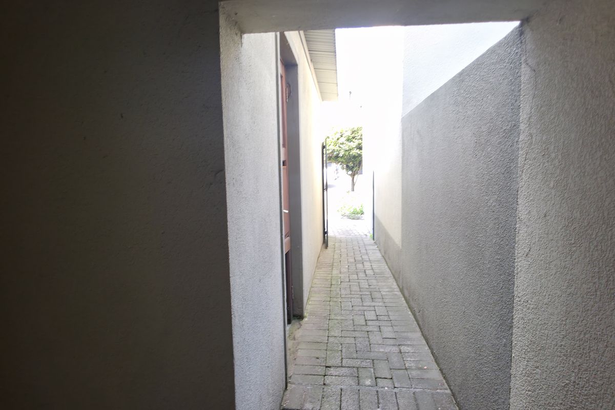 A narrow paved side passage or walkway leading to the rear garden area of the townhouse.
