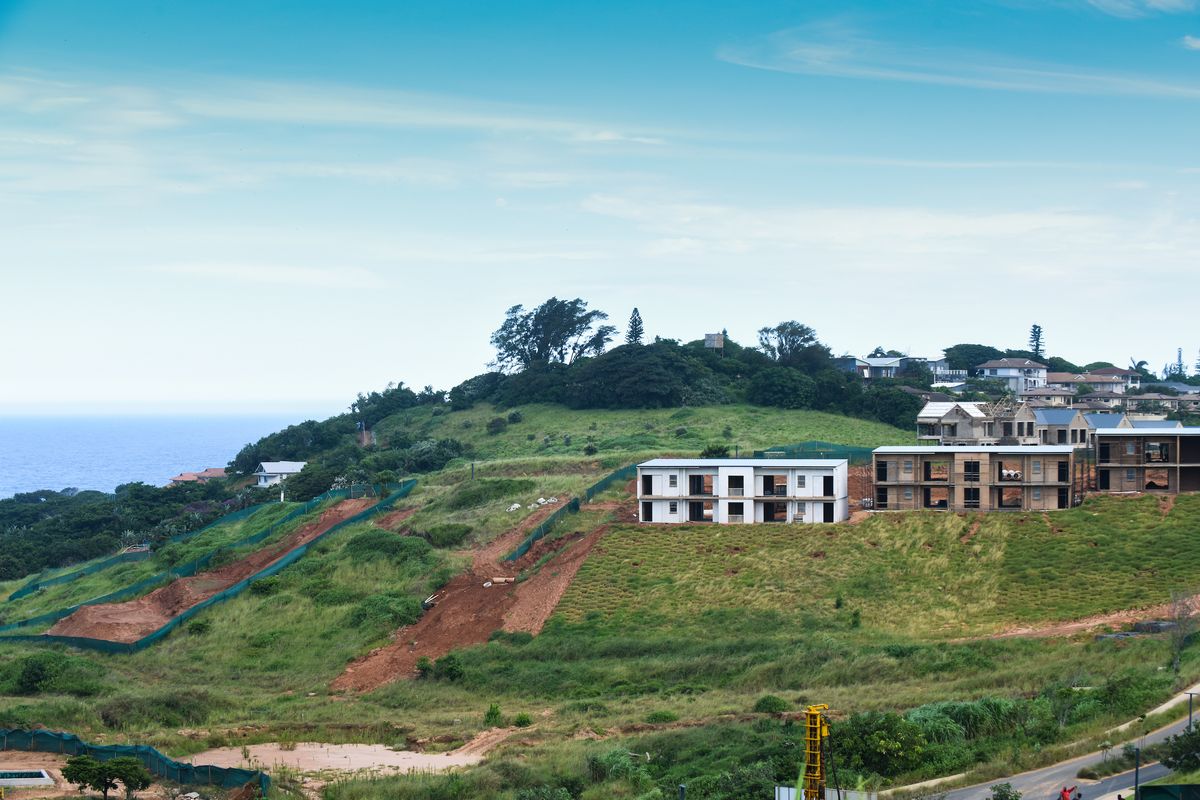 An aerial view of a residential development site on a coastal hillside, showing ongoing construction and earthworks.