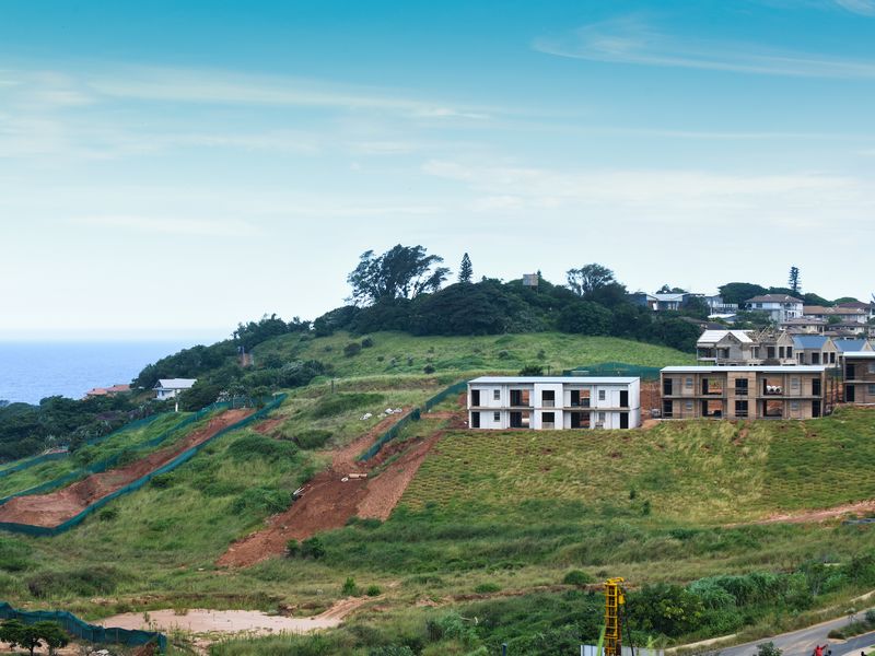 An aerial view of a residential development site on a coastal hillside, showing ongoing construction and earthworks.