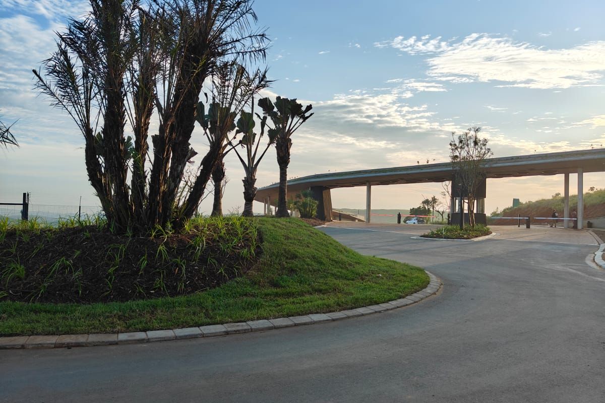 A well-maintained entrance area featuring a paved driveway, landscaped garden beds, and a modern security gatehouse structure.