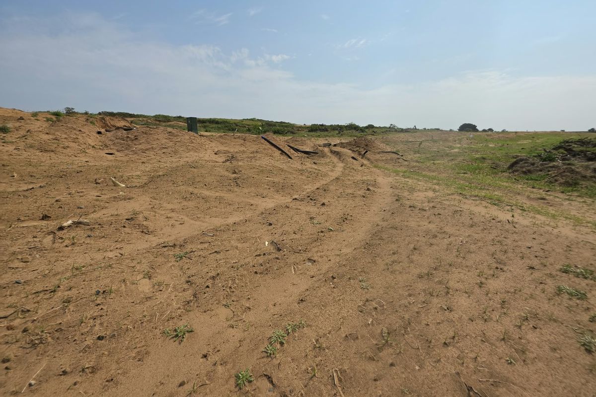 A wide-angle view of a vacant residential plot featuring sandy, uneven terrain and a utility box, ready for future development.
