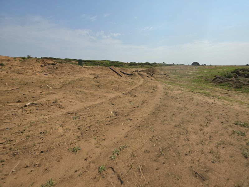 A wide-angle view of a vacant residential plot featuring sandy, uneven terrain and a utility box, ready for future development.