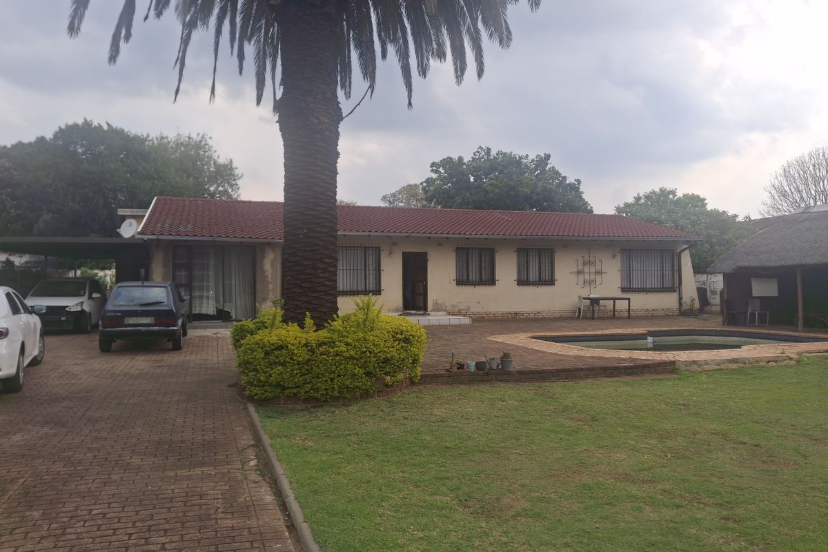 Rear view of the property featuring a paved patio, swimming pool, thatched lapa, and a large palm tree set within a spacious garden.