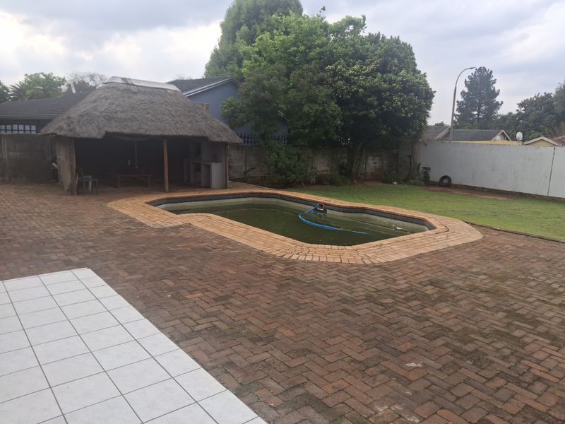 Outdoor entertainment area featuring a swimming pool, a thatched lapa, and extensive brick paving in a private garden setting.