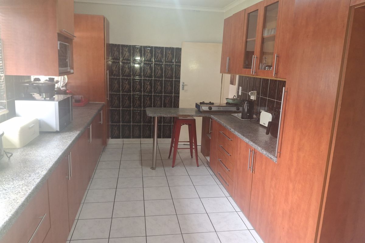 A functional kitchen featuring wood-look laminate cabinetry, granite countertops, tiled backsplash, and a built-in breakfast bar with ceramic tile flooring.