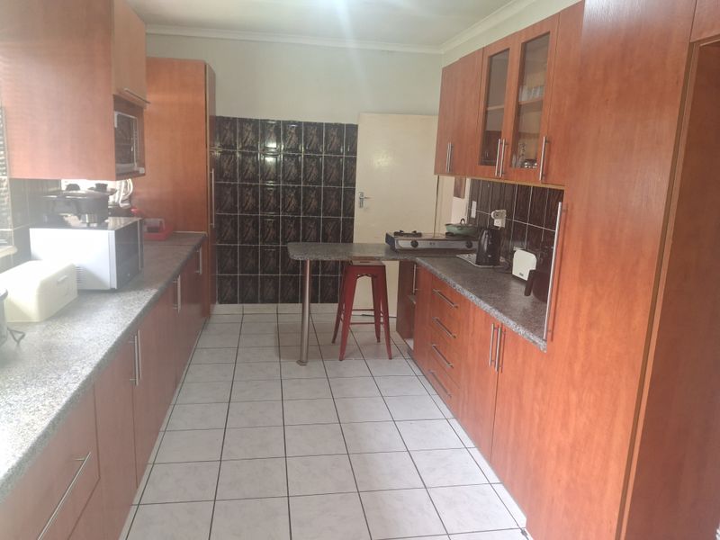A functional kitchen featuring wood-look laminate cabinetry, granite countertops, tiled backsplash, and a built-in breakfast bar with ceramic tile flooring.