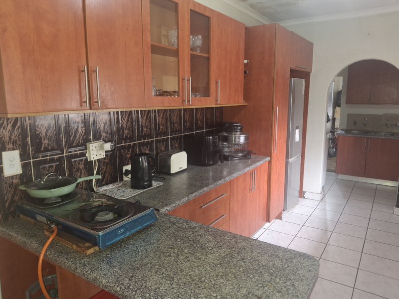 A functional kitchen featuring wood-look cabinetry, granite countertops, and a tiled backsplash, with an adjoining scullery area visible through the archway.