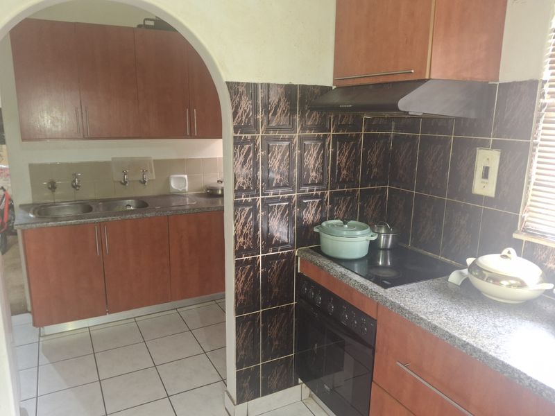 A functional kitchen featuring wood-finish cabinetry, granite countertops, a built-in oven with hob, and a separate scullery area with a double sink.