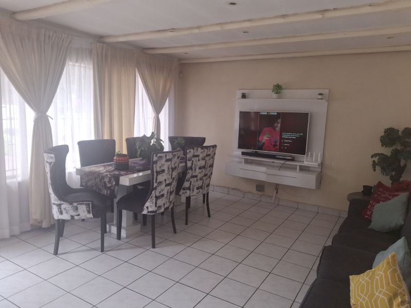 Open-plan living and dining area featuring tiled flooring, exposed beam ceilings, and a built-in media console unit.