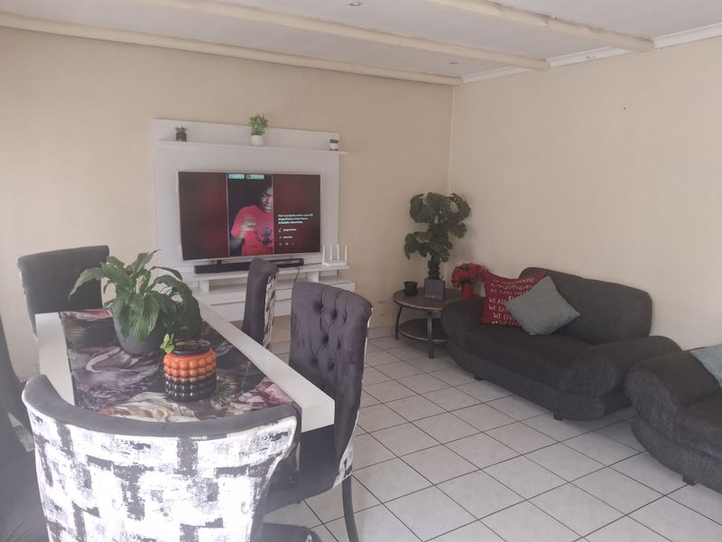 A living room featuring tiled flooring, exposed ceiling beams, and a built-in media unit, offering a functional space for relaxation and entertainment.