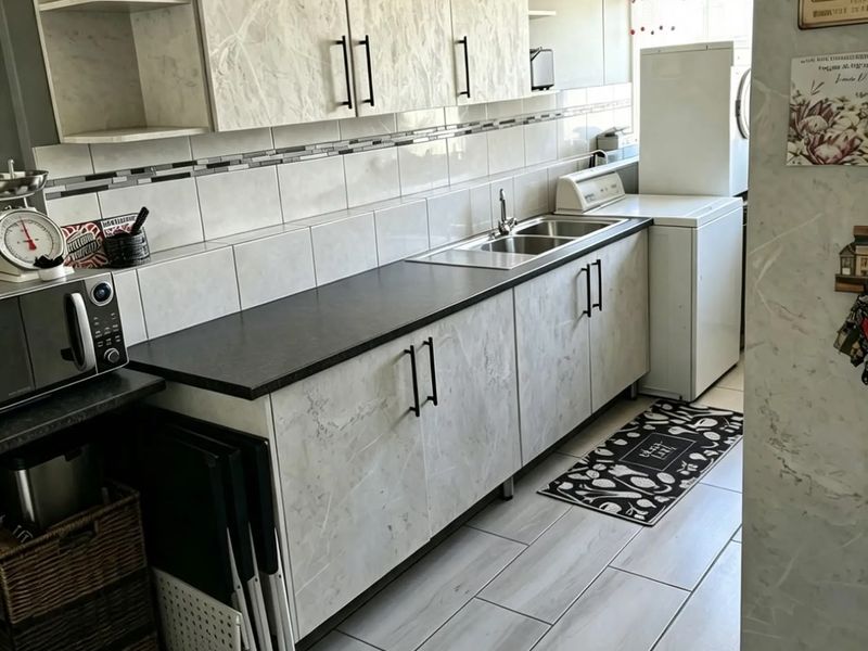 A functional kitchen featuring marble-effect cabinetry, dark countertops, a stainless steel sink, and modern tiled flooring with a clean, neutral aesthetic.