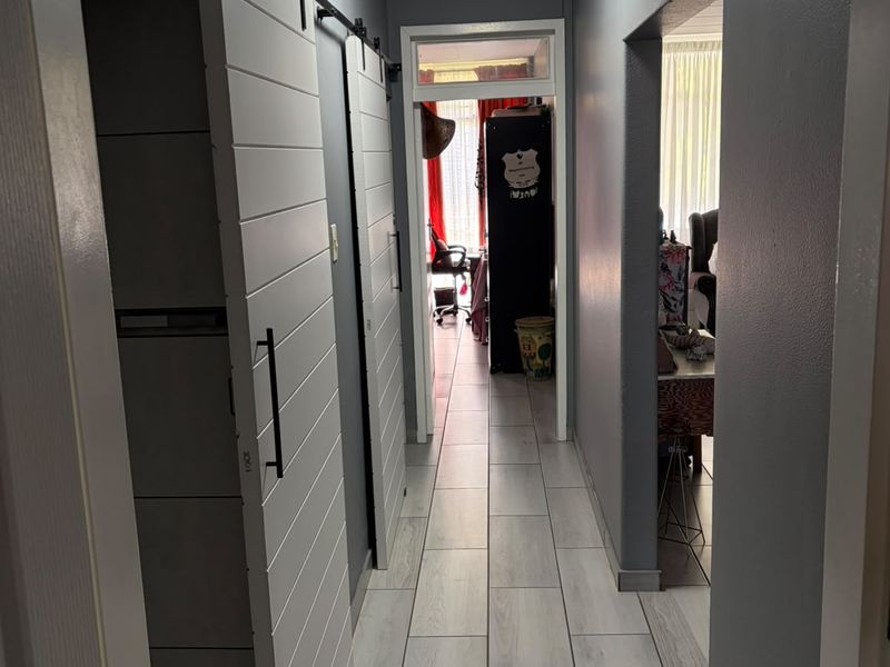 A well-lit hallway featuring modern light-toned tiled flooring and sliding barn-style doors, providing a clean and functional transition between living spaces.