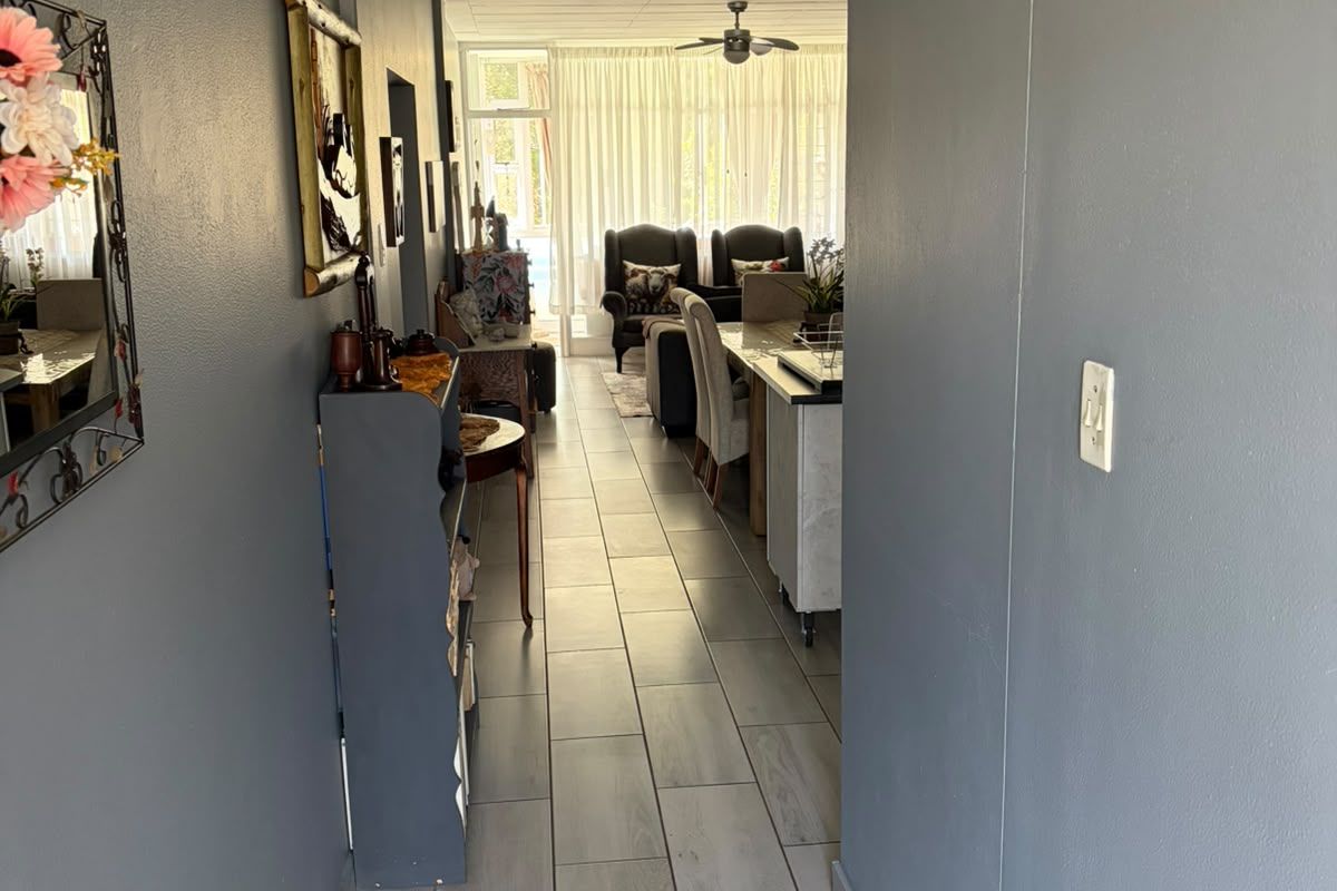 A view through a hallway with grey tiled flooring leading into an open-plan living and dining area with natural light.