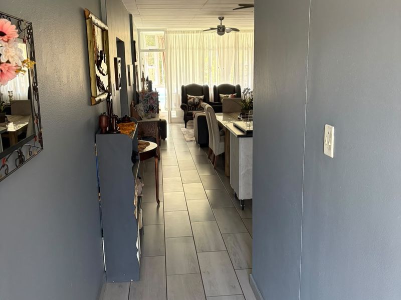 A view through a hallway with grey tiled flooring leading into an open-plan living and dining area with natural light.