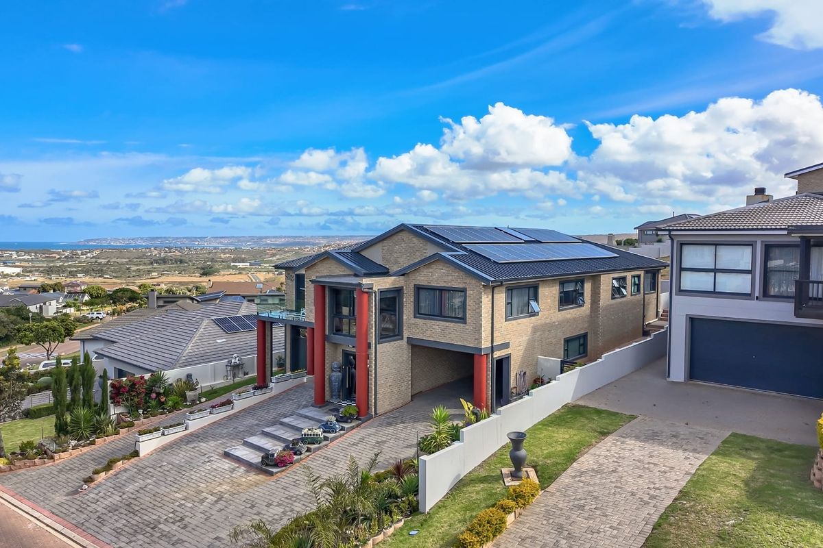 Aerial view of a modern double-story brick house featuring a paved driveway, solar panel installation, and expansive coastal landscape views.