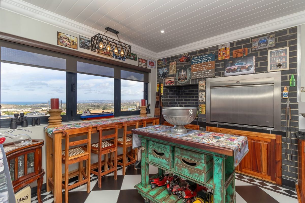 A unique kitchen area featuring a built-in stainless steel braai, black brick wall, checkerboard flooring, and expansive windows with scenic coastal views.
