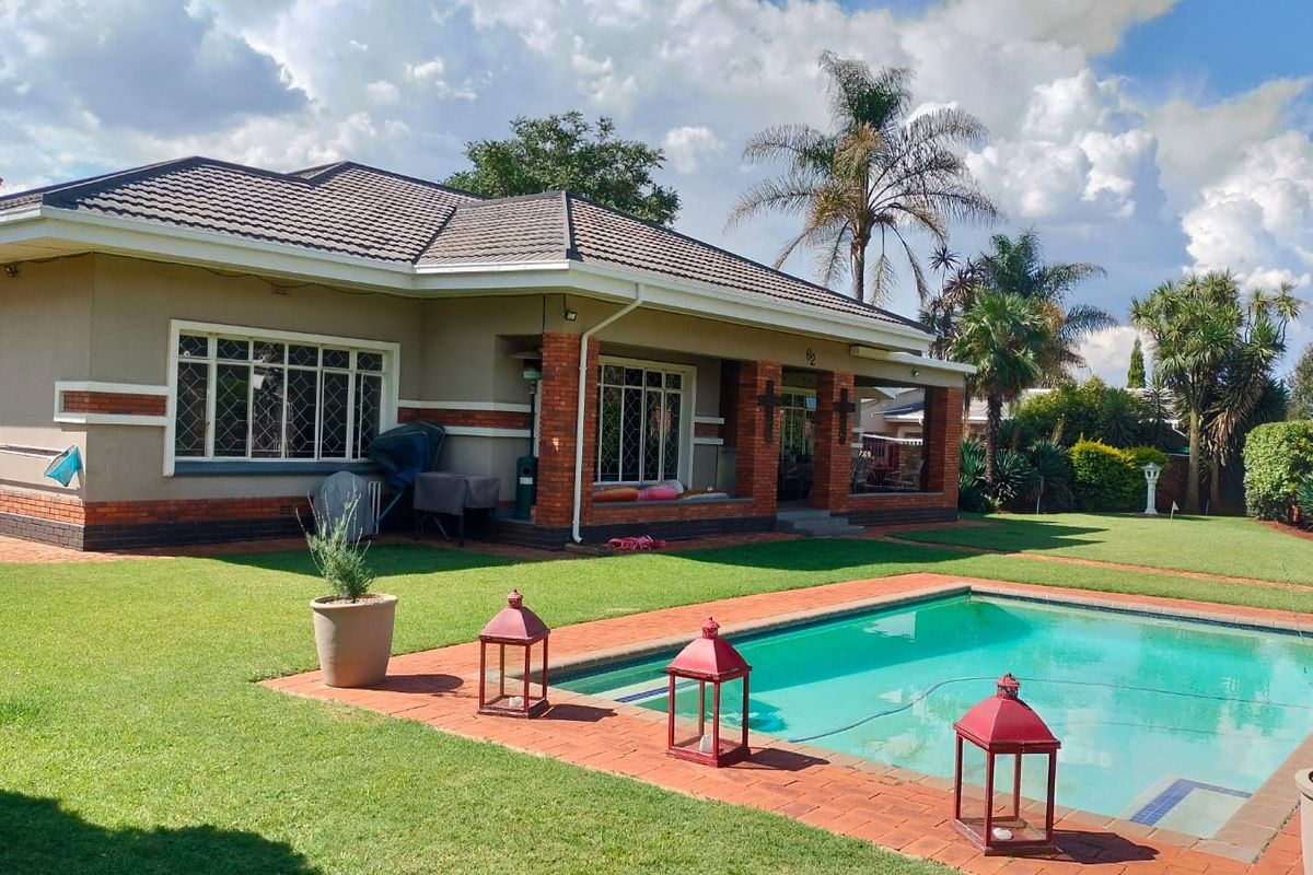 A well-maintained rear exterior view featuring a swimming pool, brick-paved patio area, and a covered veranda attached to the main house structure.