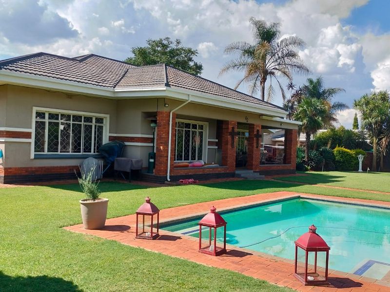 A well-maintained rear exterior view featuring a swimming pool, brick-paved patio area, and a covered veranda attached to the main house structure.