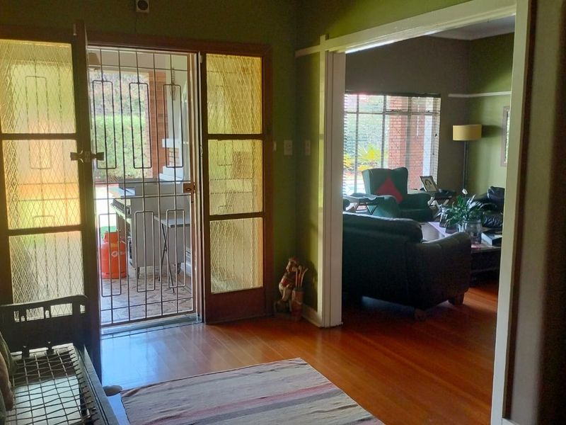 Entrance hall featuring polished hardwood flooring, a security gate, and a timber-framed glass door leading to the outdoor area.