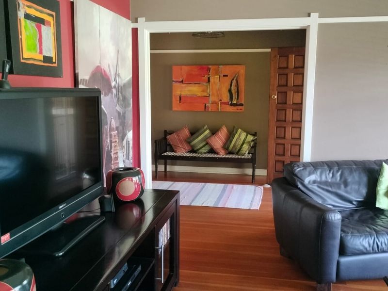 A living room featuring hardwood flooring and a classic timber panel door leading to an adjacent space, finished with neutral and accent wall tones.