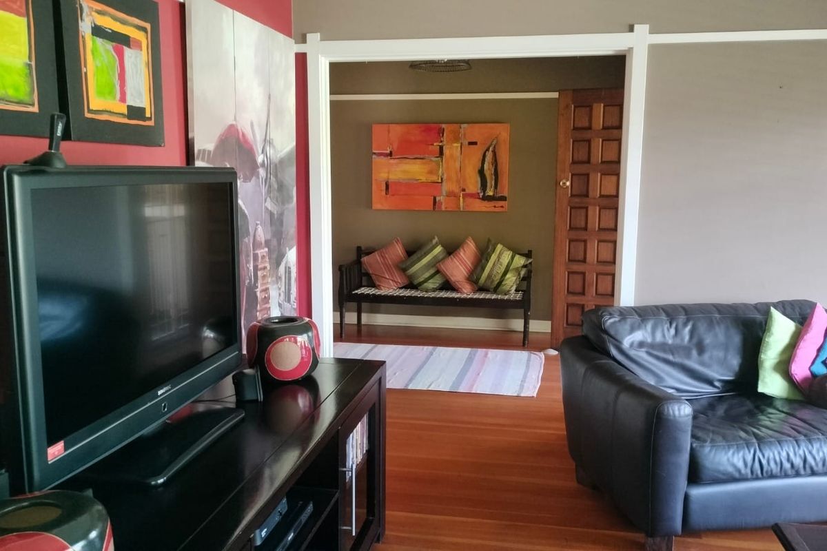 A living room featuring hardwood flooring and a classic timber panel door leading to an adjacent space, finished with neutral and accent wall tones.