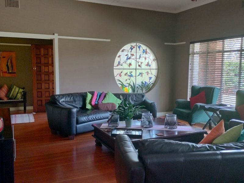 Spacious living room featuring polished hardwood flooring, a unique circular stained glass window, and large windows with venetian blinds.