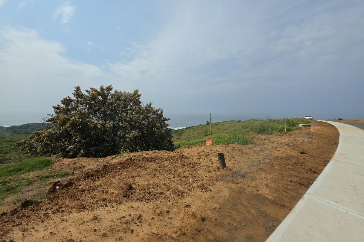 A vacant residential land plot featuring a coastal view, concrete curbing, and natural landscape.