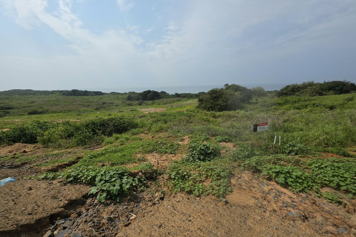 A wide-angle view of a vacant residential plot featuring natural coastal vegetation and open landscape.