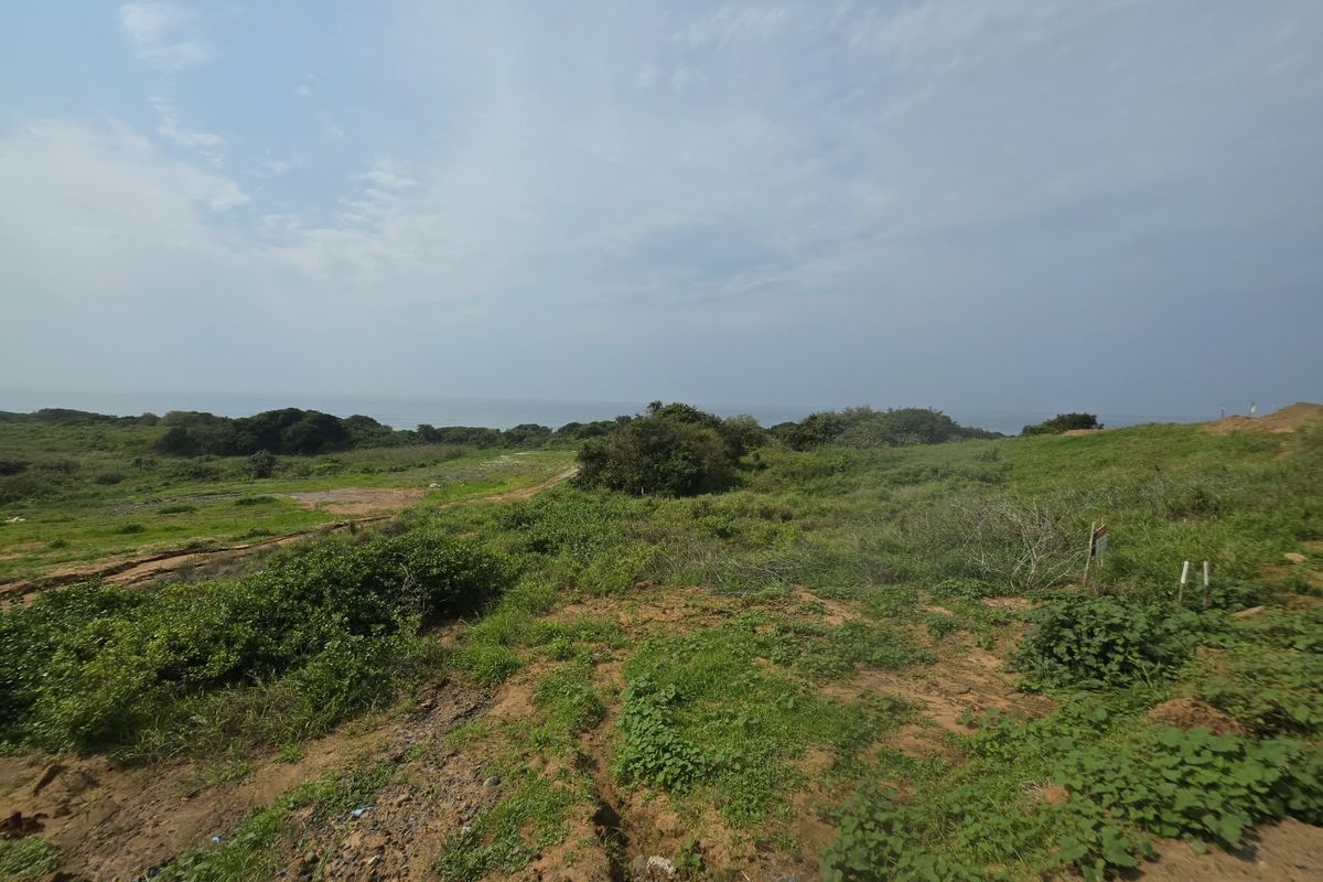 A wide-angle view of the vacant residential land featuring natural coastal vegetation and distant ocean views.