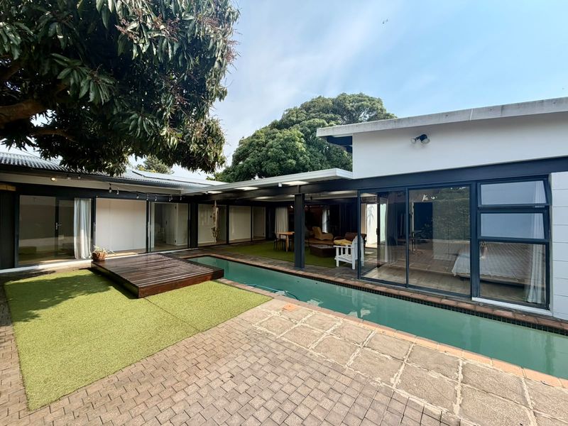 Outdoor pool area featuring a lap pool, timber deck, paved patio, and covered veranda with direct access to the home through sliding glass doors.